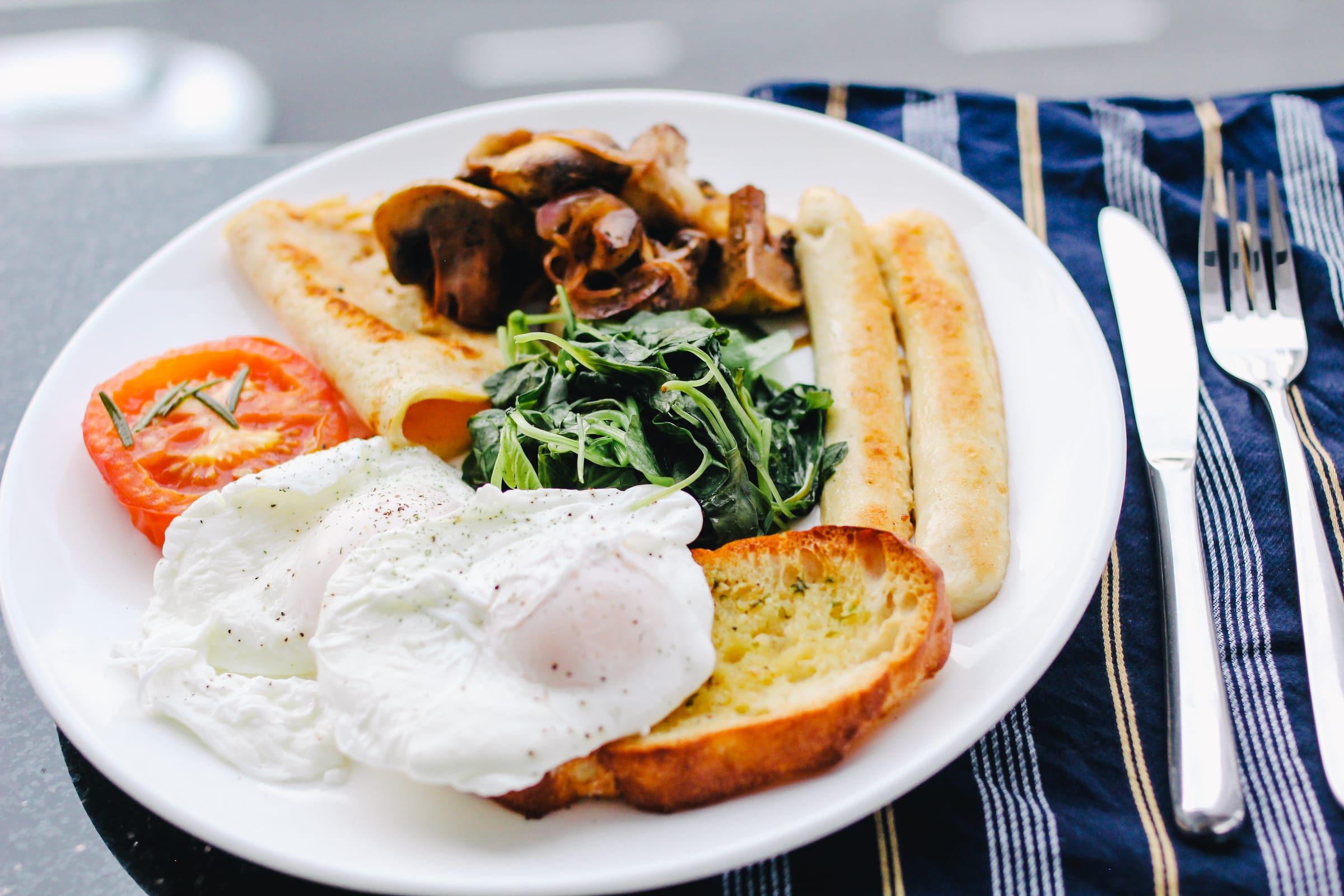 Poached eggs, sausages, mushrooms, spinach, roast tomato and toast on a white plate