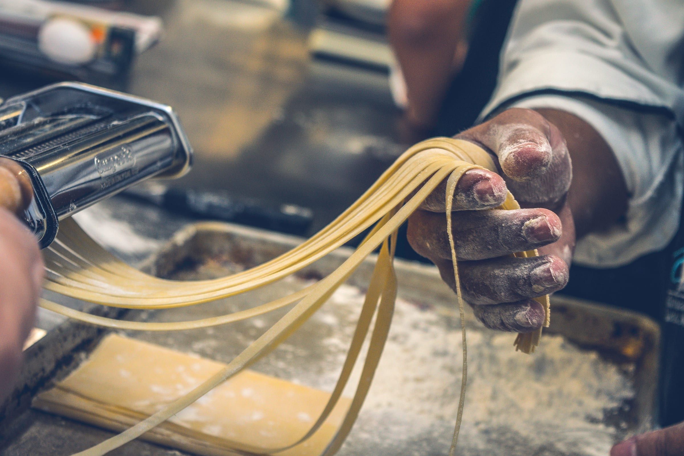 Hands feeding fresh pasta dough through a hand-cranked machine