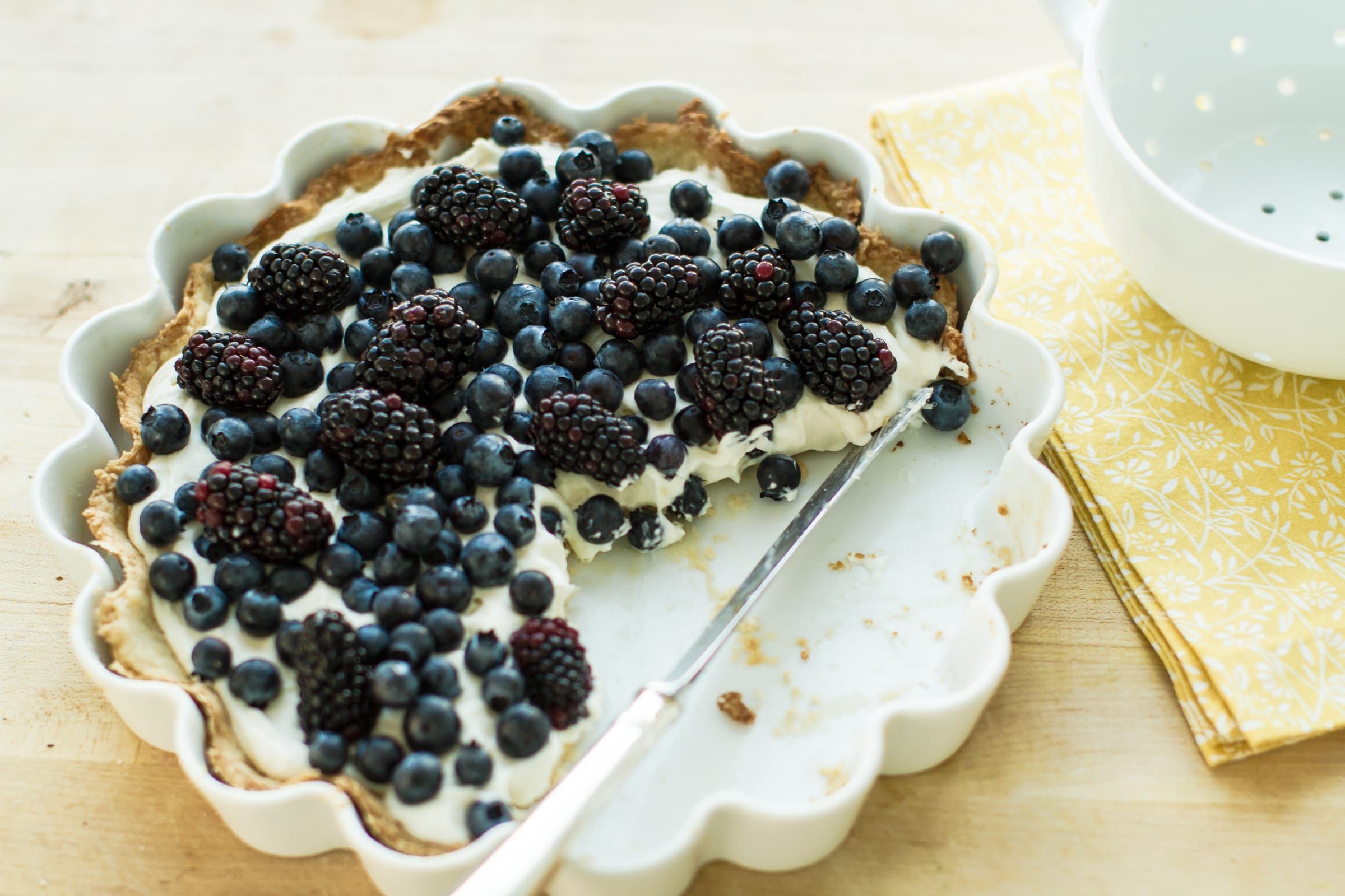 A berry cream tart in a white fluted dish, one slice taken