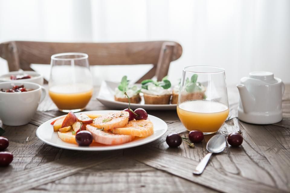 Fruit, toasts, orange juice and a teapot across a breakfast table