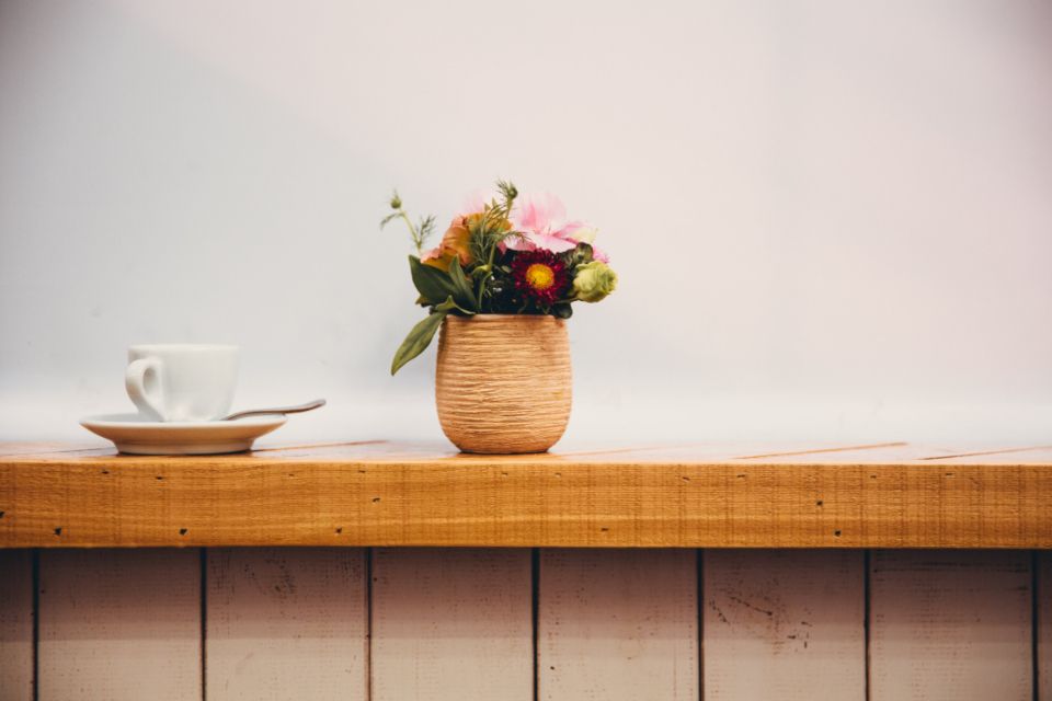 A small pot of flowers and a coffee cup on a pale wooden counter