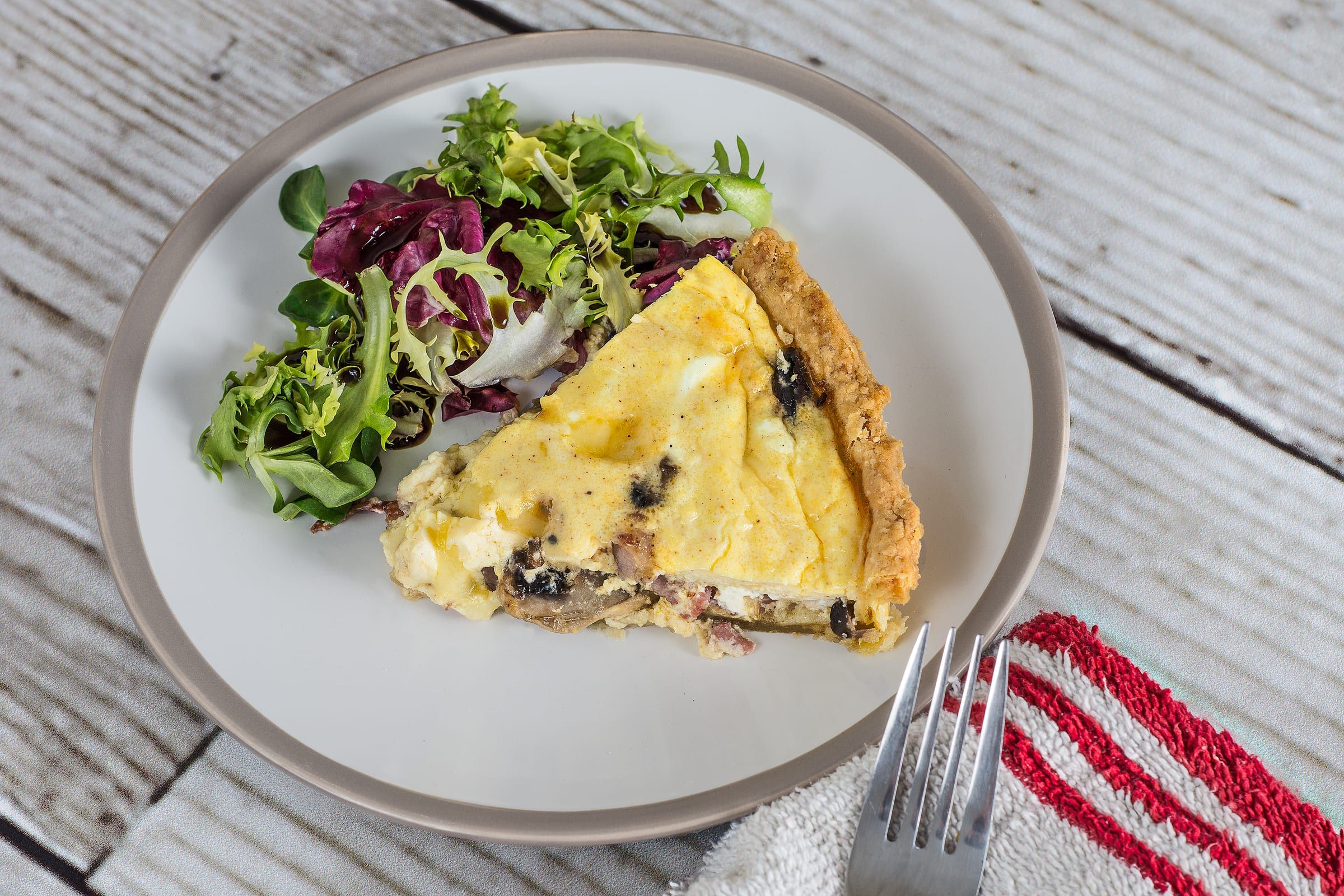 A slice of quiche with a leafy salad on a white plate