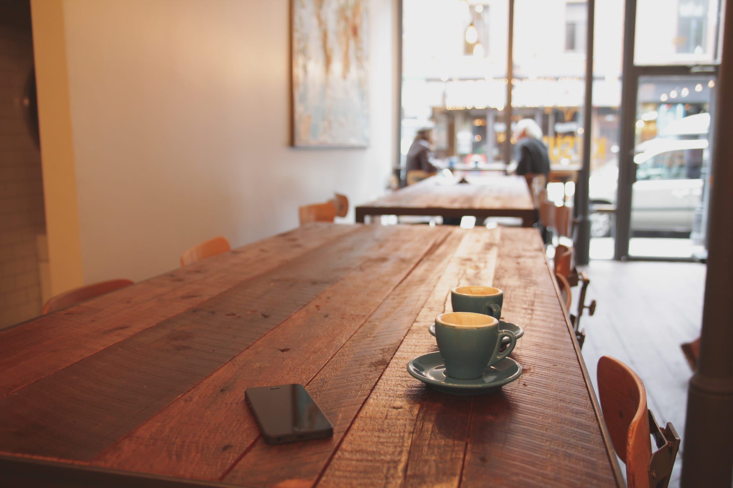 A long wooden table by the front windows, two cups of coffee in the morning light