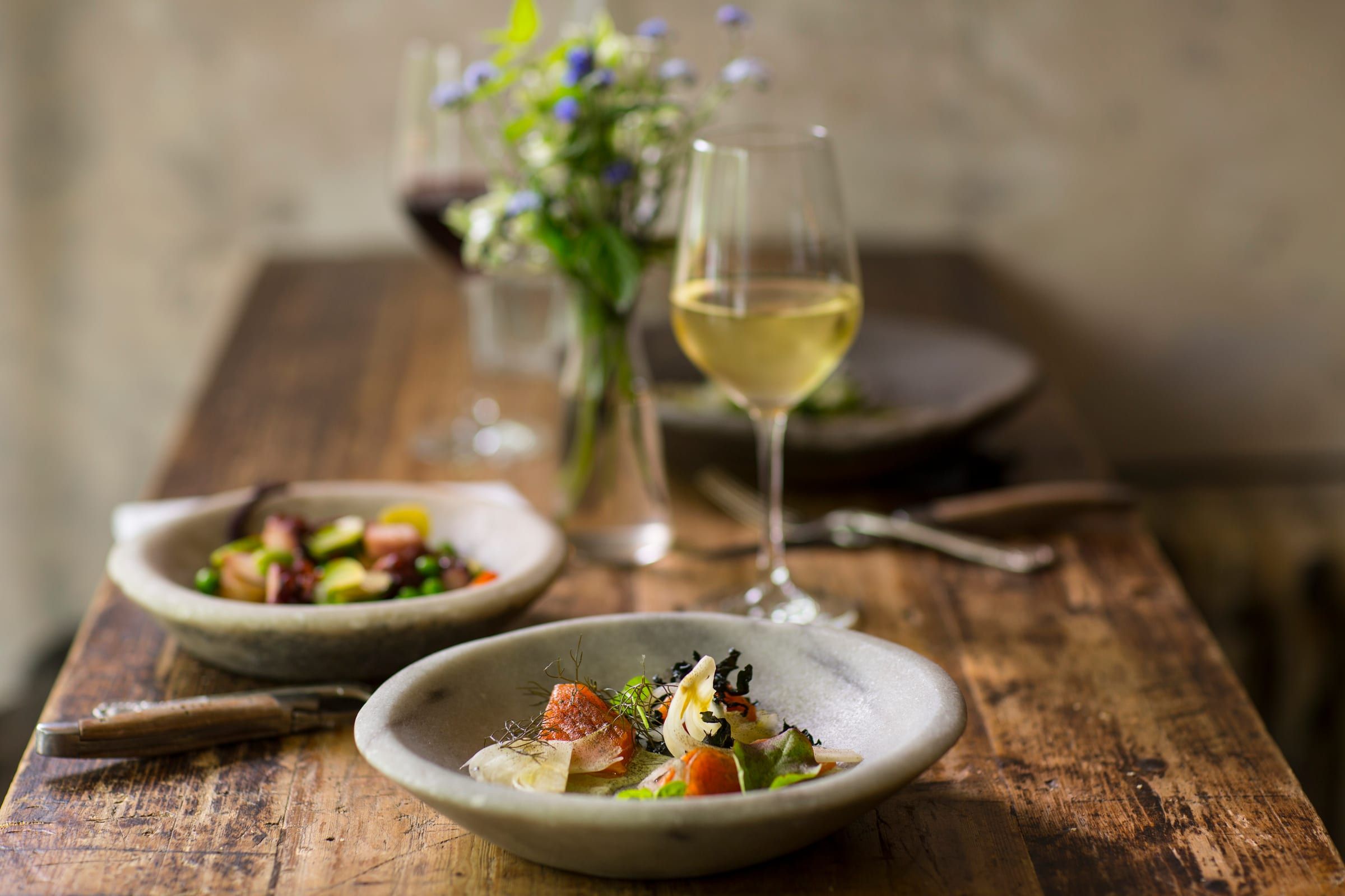 A glass of white wine and two small plates on a wooden table